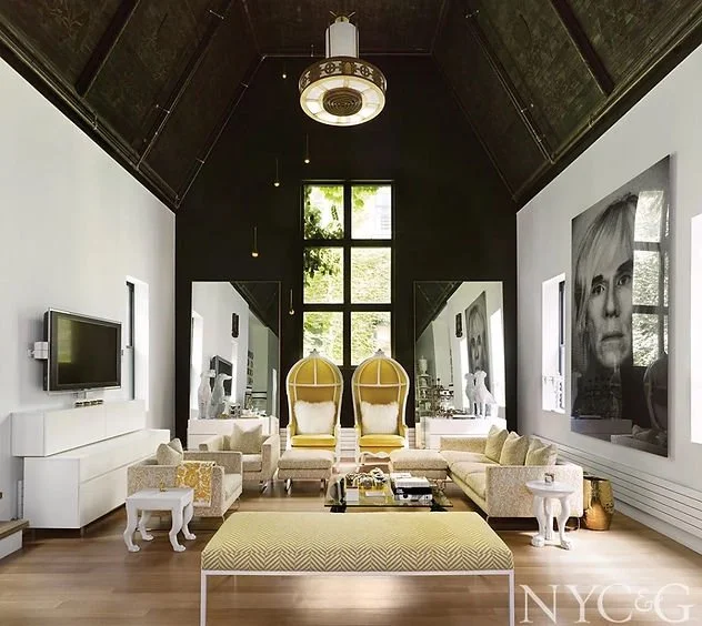 Modern living room with high ceiling, large windows, contemporary furniture including two yellow chairs, and a large black-and-white portrait on the wall.