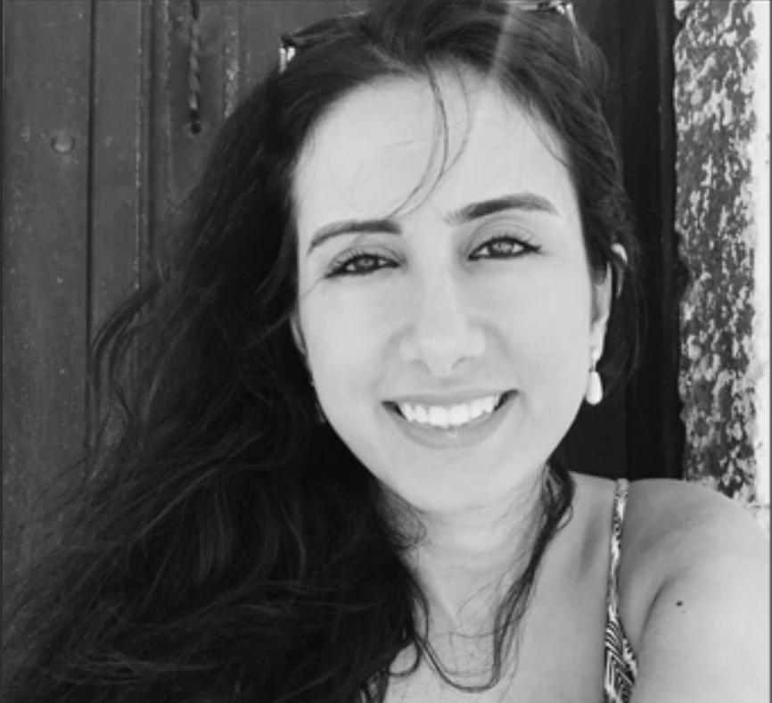 Woman smiling, wearing earrings, and a patterned top