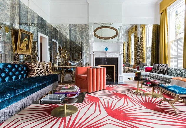Eclectic living room with a mix of traditional and modern decor, featuring a bold red and white patterned rug, blue velvet sofa, leopard print cushions, marble walls, and gold accents. A fireplace with a mirror above and bright orange and blue chairs add color. Large windows with mustard curtains allow natural light.