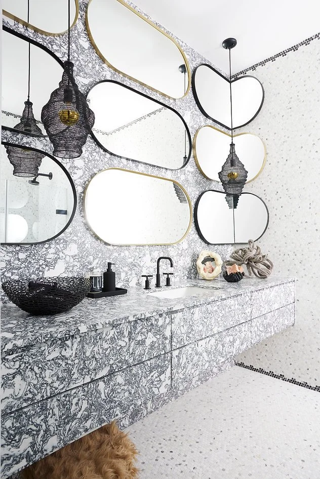 Modern bathroom with patterned marble countertop, black faucet, decorative mirrors, pendant lights, and black accessories.