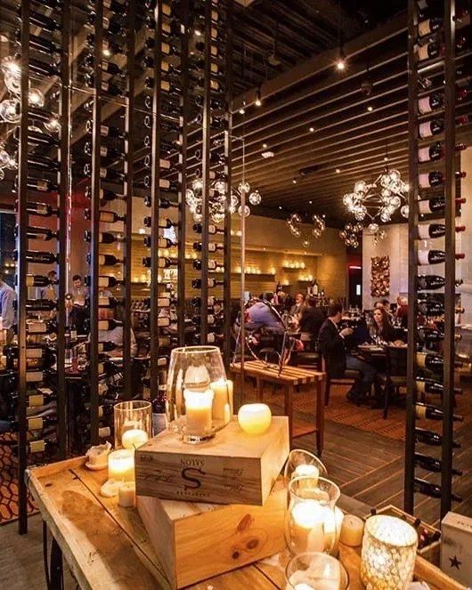 Houston hospitality interior design at Vallone’s showcasing dramatic wine wall, statement lighting, and refined restaurant dining space.