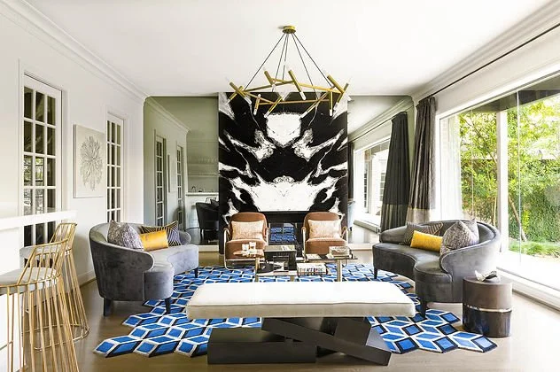 Modern living room with geometric blue rug, gray sofas, large abstract art, and gold chandelier.