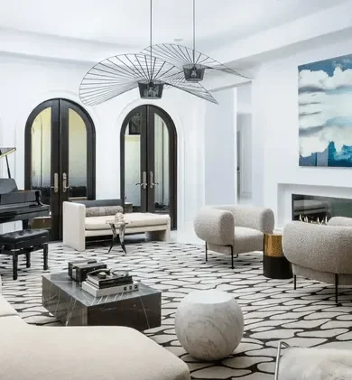 Modern living room with black framed arched doors, white and beige furniture, black and white patterned rug, abstract wall art, and unique ceiling décor.