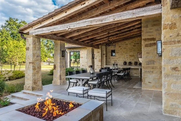 Outdoor patio with stone pillars, a covered seating area, dining tables and chairs, and a modern fire pit.