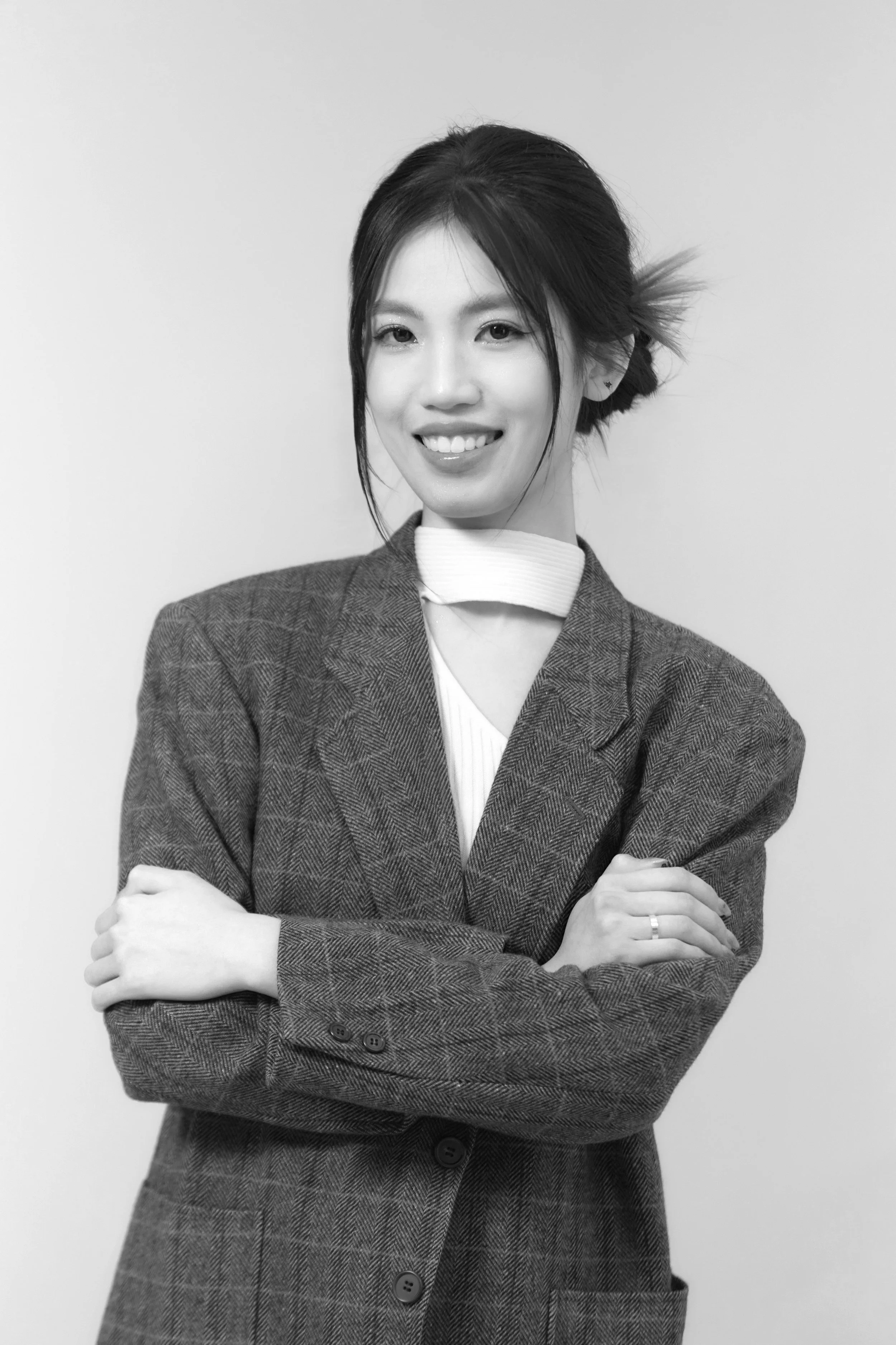 Black and white portrait of a woman with short hair, smiling, wearing a blazer and a high-neck top, with arms crossed against a plain background.