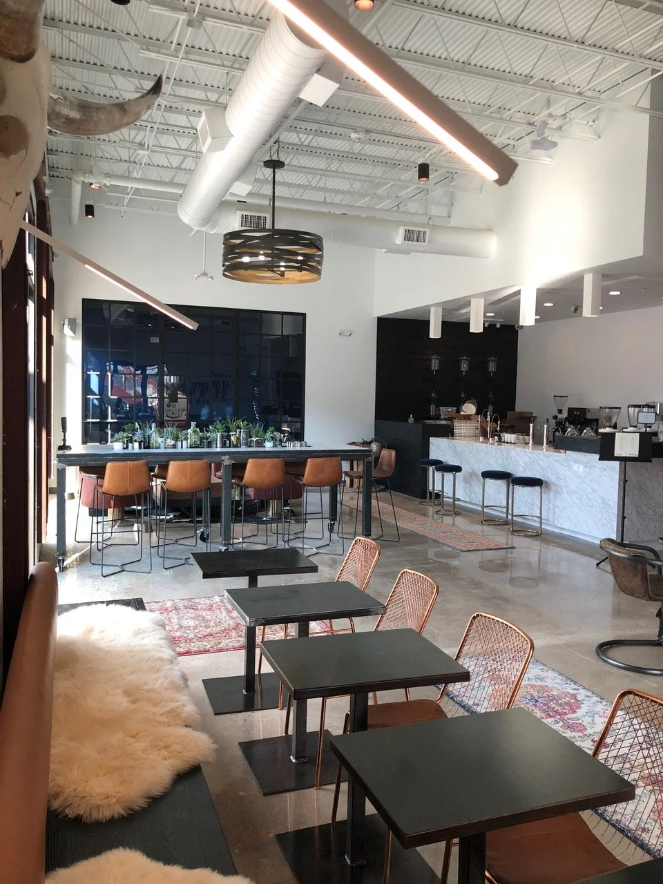 Cafe interior in Rice Village Houston showing hospitality-focused commercial interior design with marble bar, mixed seating, and warm industrial finishes.