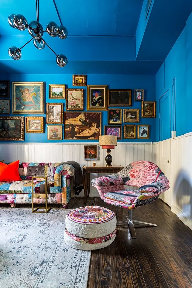 Eclectic living room with blue walls, a gallery of framed art, a patchwork couch, and a patterned chair and ottoman.