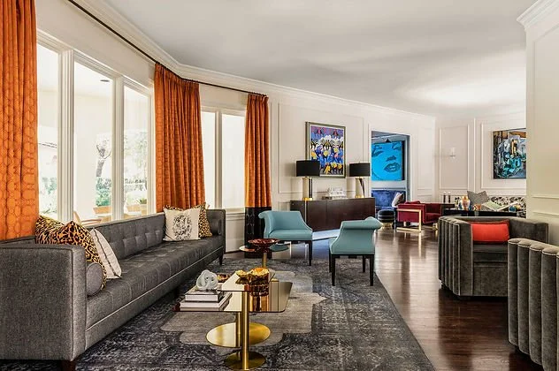 Modern living room with gray sofas, orange curtains, and colorful artwork.